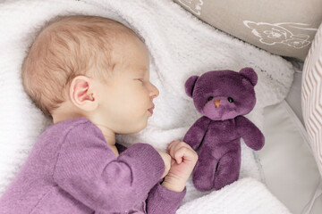 Cute newborn baby girl sleeps at home in her crib with her favorite toy, the first month of life