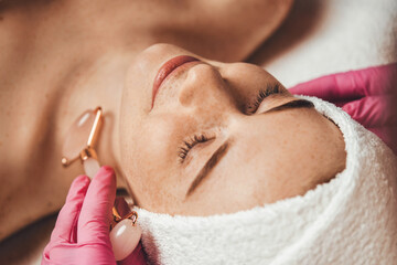 Wall Mural - beautician massaging face of woman patient with jade roller during spa session. natural beauty. beau