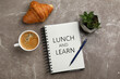 © New Africa - Lunch and Learn concept. Notebook, cup of aromatic coffee, delicious croissant and plant on brown marble table, flat lay