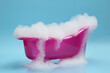 Toy bathtub overflowing with foam on light blue background