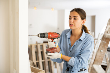 Woman drilling hole in wall with screwdriver in a repairable room