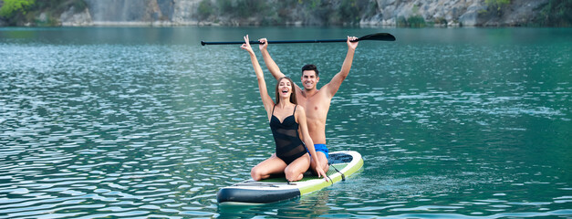 Wall Mural - Happy young couple using paddle board for sup surfing in river