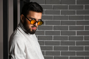 Canvas Print - Young bearded man wearing stylish sunglasses near grey brick wall