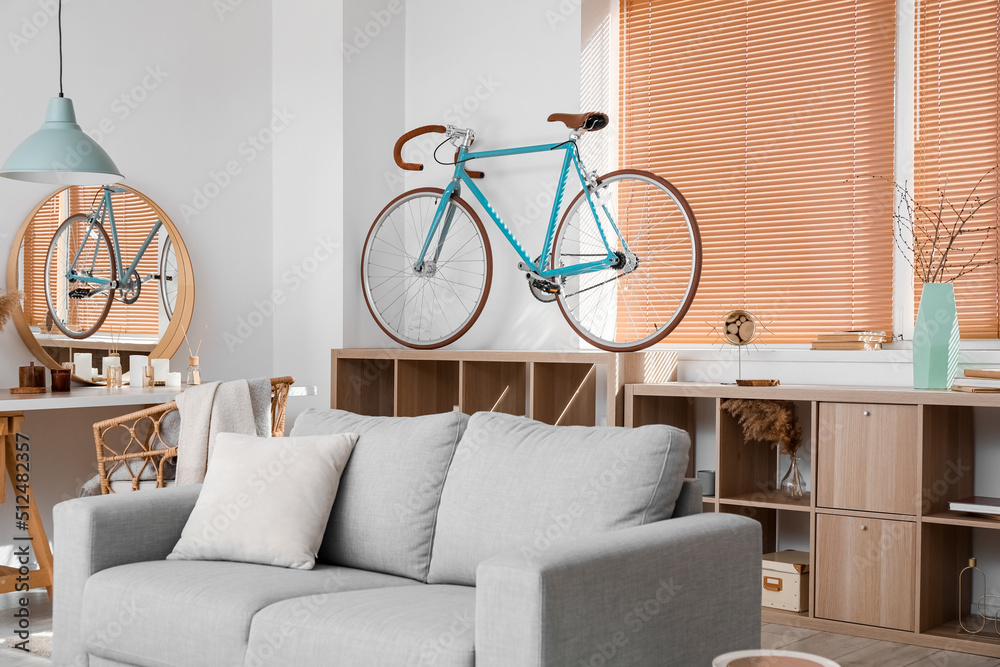 Interior of modern living room with bicycle, shelving unit and grey sofa