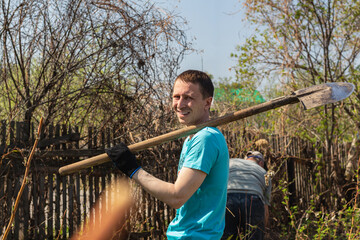 Two positive male gardeners with farm tools near old wooden fence at sunny day