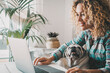 People working on computer with dog on the legs. Happy woman animal owner using laptop for work or surf the web. Adorable pug puppy looking his human best friend while he write on notebook.Lifestyle