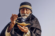 An old Arabic sorcerer holds an Aladdin's lamp and conjures.