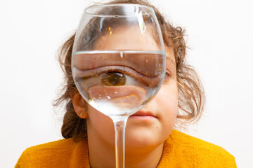 Fashion kid portrait, eye looks through the glass of water. Object distortion, optical illusion concept. Minimalist contemporary art. high quality photo