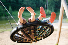 Kids Swinging On Wicker Swing On Playground In Park By Lake, Children's Summer Vacation With Friends