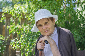 Portrait of an elderly woman in a white panama against a background of green foliage.