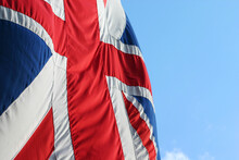 A UK Union Flag, Aka Union Jack, In Movement On A Windy Day With Blue Sky Copy Space.