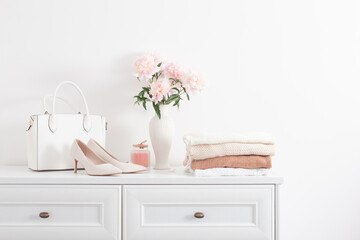 white dresser with clothes and flowers in white room