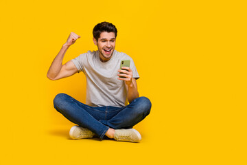 Poster - Full body photo of hooray brunet millenial guy sit hold telephone wear t-shirt jeans sneakers isolated on yellow background