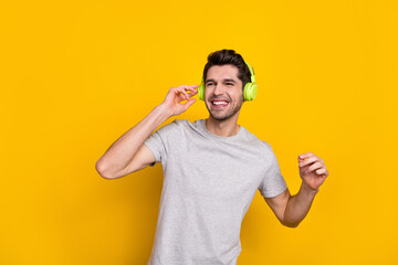 Poster - Photo of funny brunet young guy enjoy music look up wear earphones grey t-shirt isolated on yellow color background