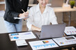 © aksonsat - Business women are discussed on paperwork that show accounting numbers tables and working on laptop in office space.