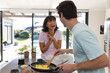 © Wavebreak Media - Caucasian young man talking with cheerful asian girlfriend while making scrambled eggs in kitchen
