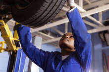 African American Mid Adult Female Mechanic Examining Car's Tire In Workshop