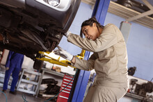 Side View Of Mid Adult Asian Female Engineer Examining Faulty Car In Workshop, Copy Space