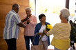 © wavebreak3 - Biracial seniors receiving cheerful friends with bouquet and champagne bottle in nursing home