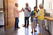 © WavebreakMediaMicro - Biracial seniors receiving friends with bouquet and champagne bottle in nursing home, copy space