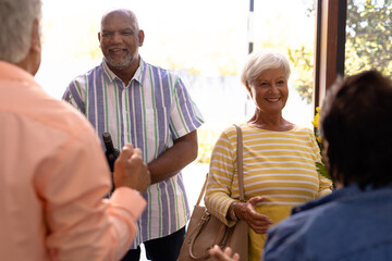 Wall Mural - Biracial seniors welcoming cheerful friends standing at doorway in nursing home, copy space