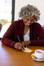 Smiling African American Senior Woman Marking Off Numbers On Bingo Card Over Dining Table