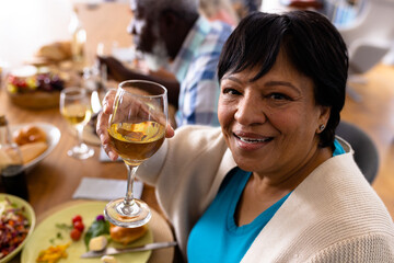 Wall Mural - Portrait of multiracial senior woman enjoying wine while having lunch with friend at dining table