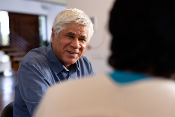 Smiling biracial senior man talking with female friend while sitting for lunch in nursing home