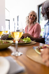 Wall Mural - Cheerful multiracial senior couple holding hands while having lunch at dining table in nursing home