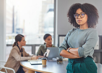 Poster - Were on the move. Portrait of a young businesswoman folding her arms while her colleagues have a meeting in the background.