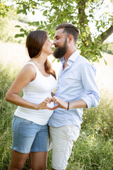 Wall Mural - pretty young pregnant woman with white shirt stands with her boyfriend with beard and blue shirt in high flower meadow and cuddle