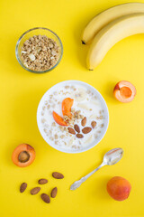 Wall Mural - Granola breakfast with milk, fruits and almonds in the white bowl on the yellow background. Top view. Location vertical.