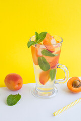 Wall Mural - Infused water with apricot and mint in the drinking glass on the yellow  background. Closeup. Location vertical.