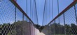 Outdoor hanging suspension bridge structure made with iron metal cable rope and tower for crossing green forest lake water. Empty and quiet forth deck walkway or path close up view under daylight