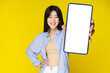 © Svyatoslav Lypynskyy - Asian girl holding smartphone showing white screen, and excited smile on camera wearing blue shirt isolated on yellow background. Great offer mobile app advertisement. Product placement