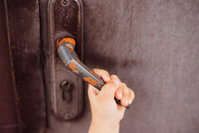 A Child's Hand Holds The Door Handle. Entering Or Leaving The House. An Old Metal Door.