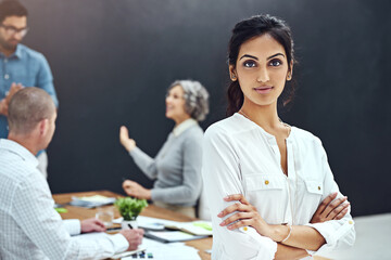 Aufkleber - Its time to get serious about our business. Portrait of a businesswoman standing with her arms folded in the boardroom while a colleague gives a presentation in the background.