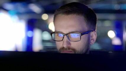 Close up view of a focused man with glasses in front of a computer.