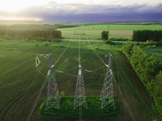 High voltage electric power tower in a green agricultural landscape at beautiful sunset