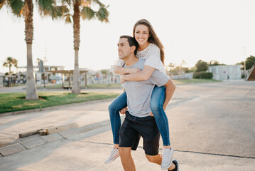 A smiling brunette girl is riding her Hispanic boyfriend between palms in Spain