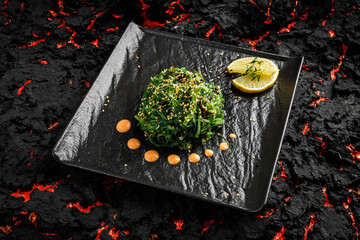 Wall Mural - fresh delicious Chukka seaweed Wakame salad ina black plate on a black stone background with limon and sauce