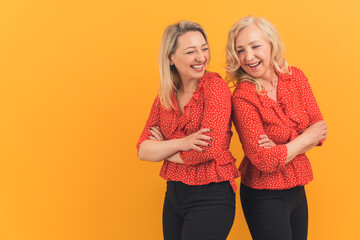 medium studio shot on yellow or orange background of two adult caucasian female friends standing bac