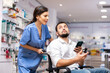 © JackF - Nurse pushing wheelchair, helping disabled man with smartphone to choose medicine.