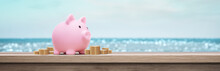 Pink Piggy Bank On The Beach With Coins On A Table - Summer Vacation Savings Concept