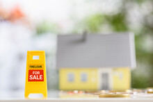 Mortgage Foreclosure Sales, Financial Concept : Yellow Warning Or Sign Board With The Words FORECLOSURE FOR SALE, A Model House And Coins On A Table, Depicting Lender Takes Possession Of The Mortgage.