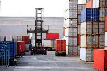 Wall Mural - Forklift truck handling cargo container boxes in logistic delivery yard with stacks of cargo containers in background.