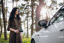 Young Beautiful Woman Traveling By Electric Car Having Stop At Charging Station Standing Plugging Cable Browsing Internet On Smartphone Smiling Joyful While Charing