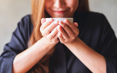 Poster - Closeup image of a young asian woman holding and drinking hot coffee