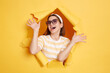© sementsova321 - Portrait of attractive happy woman wearing striped shirt and hair band posing in yellow paper hole, standing with raised arms, celebrating her victory, expressing positive emotions.