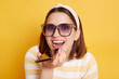© sementsova321 - Portrait of happy smiling delighted woman wearing striped shirt posing isolated over yellow background, using cell phone for recording voice message, looking at camera with excited look.